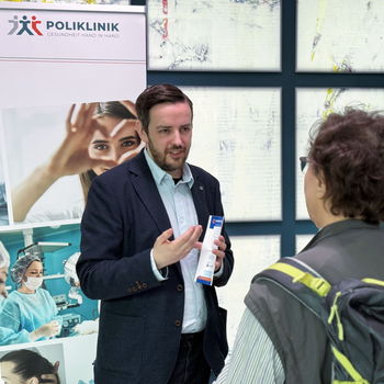 zwei Personen unterhalten sich vor Poliklinik Aufsteller