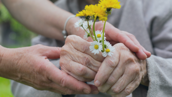 junge Person hilft einer Seniorin Blumen zu halten